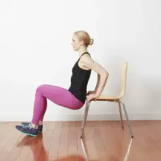 Kobieta wykonuje ćwiczenie dipy na triceps, opierając dłonie o krzesło.