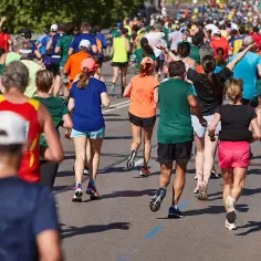Tłum biegaczy pokonuje kolejne kilometry maratonu. Widać kolorowe stroje i skupione twarze uczestników.