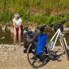Kobieta odpoczywa nad strumieniem w Beskidzie Niskim, mocząc nogi. Obok rower z sakwami, gotowy do dalszej podróży.