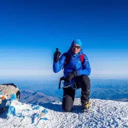 Alpinista na szczycie najwyższego szczytu Rosji, z dumą pokazuje kciuk w górę.