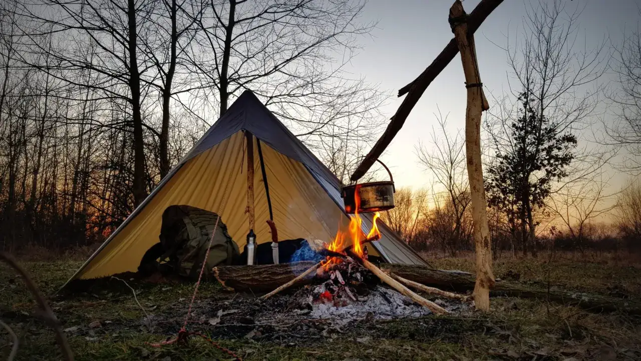 Namiot i ognisko w lesie, kociołek wisi nad ogniem. Idealne miejsce na bushcraft.