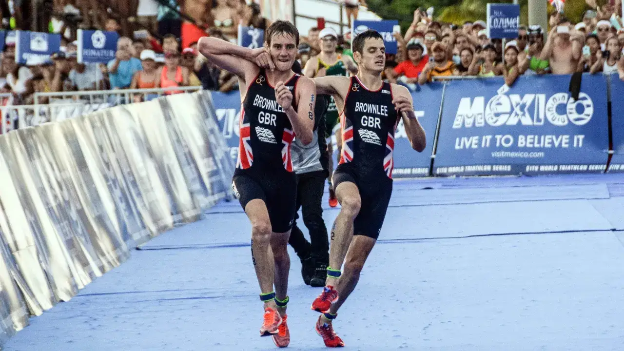 Dwóch zawodników Brownlee w strojach GBR biegnie w wyścigu triathlonowym, przypominając Iron Mana.