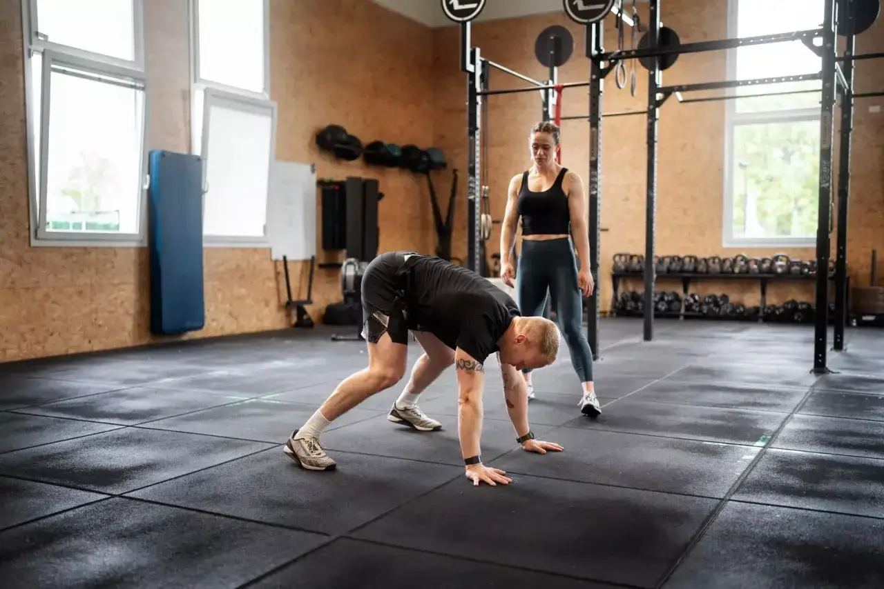 Trenerka obserwuje mężczyznę wykonującego ćwiczenie, które jest częścią treningu burpee.
