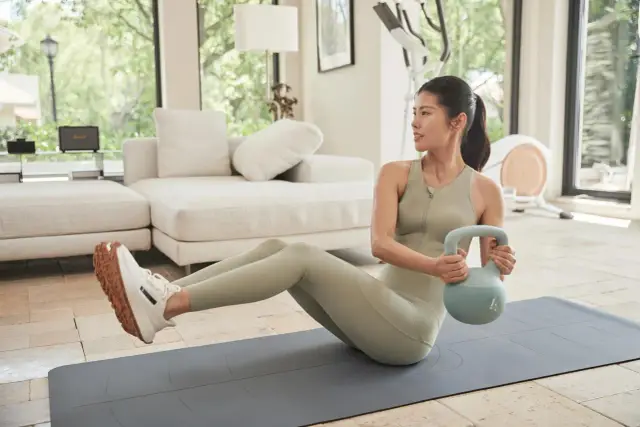 Kobieta wykonuje ćwiczenia na oponkę na brzuchu z kettlebell.
