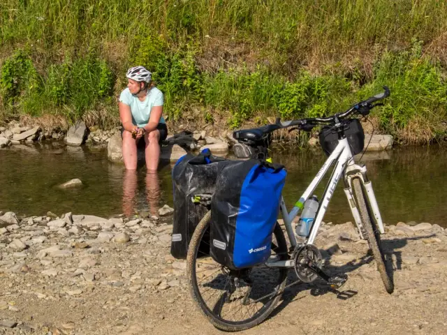 Kobieta odpoczywa nad strumieniem w Beskidzie Niskim, mocząc nogi. Obok rower z sakwami, gotowy do dalszej podróży.